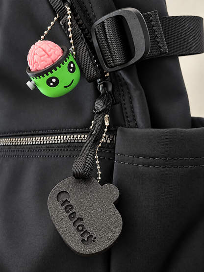 Frankie clicker beside another accessory on a black bag; bag and other accessory not included