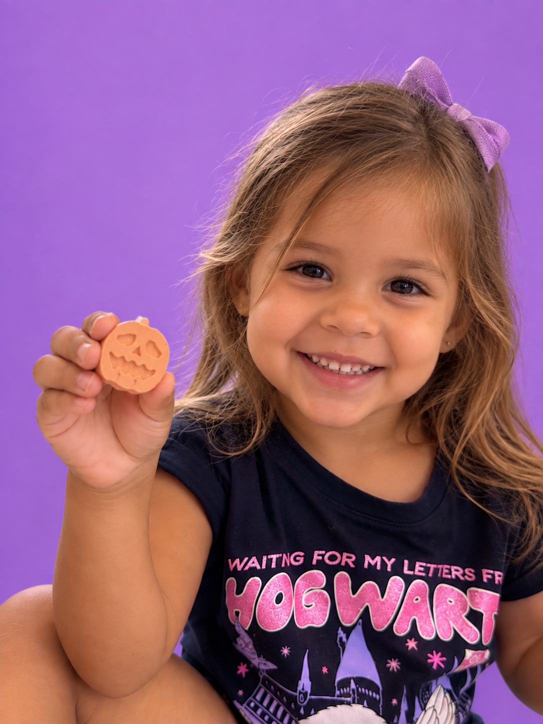 Child holding a pumpkin-shaped chalk piece against a purple background