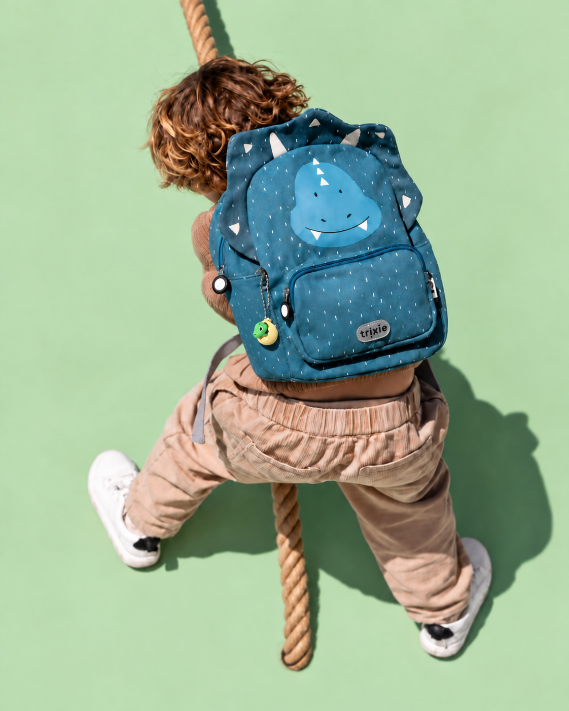 Child wearing a dinosaur backpack with the name-and-dino keychains; backpack not included
