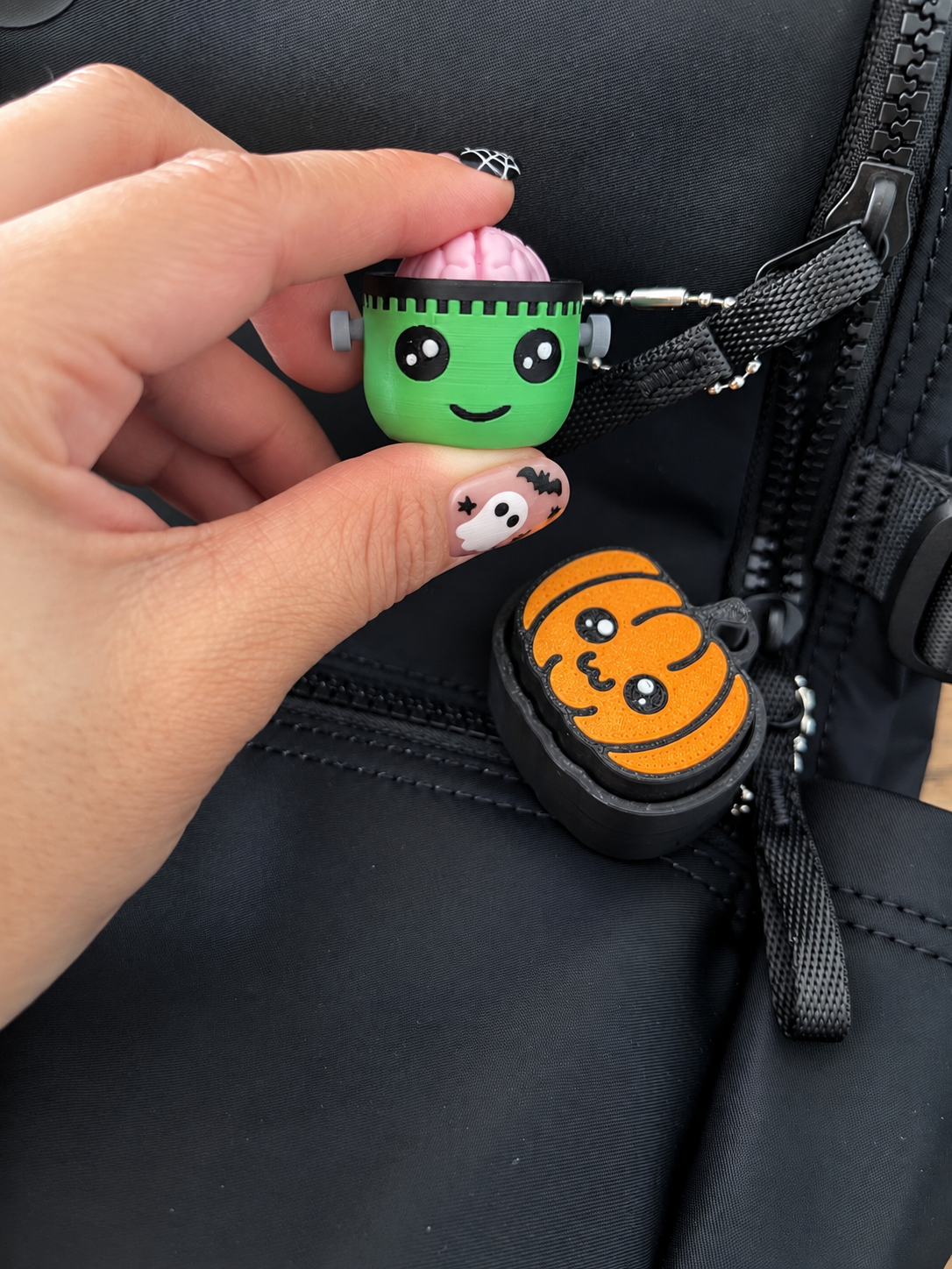 Hand pressing Frankie beside a Pumpkin Pop clicker on a black bag; bag and other clicker not included