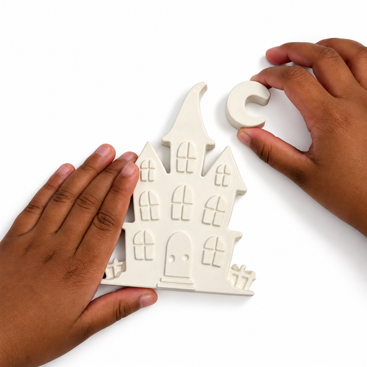 Hands beside an unpainted plaster haunted house and crescent moon